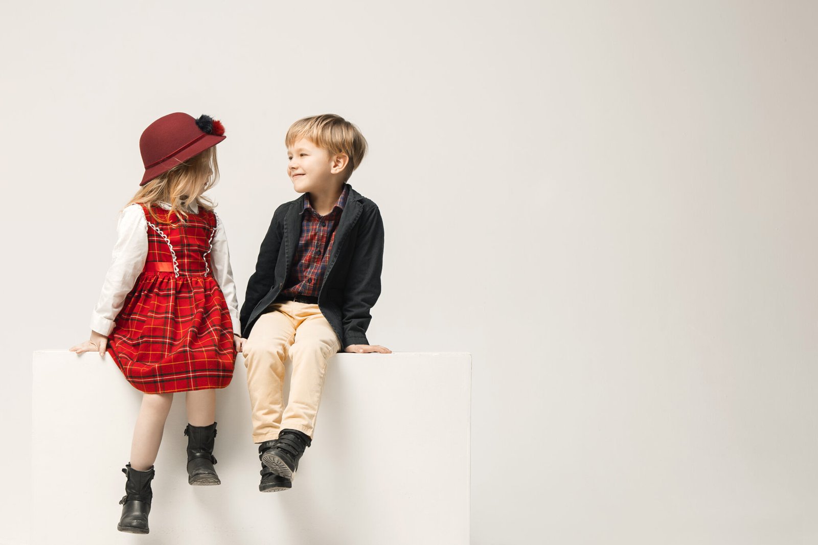 Cute stylish children on white studio background. Two beautiful teen girl and boy sittting together. Stylish young teen girl posing at studio. Classic style. Teen and kids fashion concept. children's fasion concept